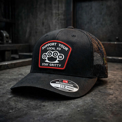 Blackout lifestyle alt: Man wearing blackout GOON Support Your Local FD Richardson 112 trucker hat driving vintage Ford truck, black on black murdered out silicone patch Firefighter Gift