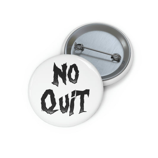 A pin button with a white background featuring the text 'NO QUIT' in black, with a metal rim and a safety pin backing.